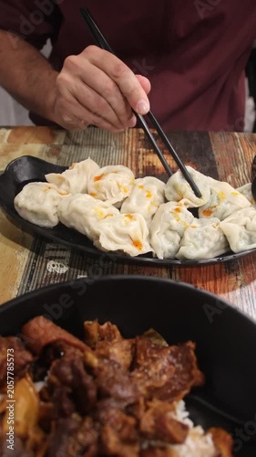 Tourist using chopsticks to eat Zong zi or steamed meat dumplings from a plate in a local restaurant serving authentic traditional Cantonese food in Hong Kong