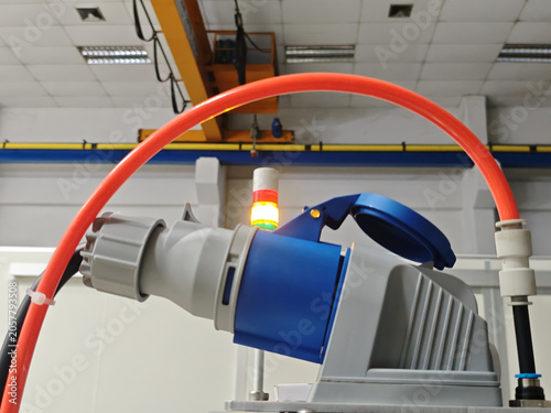 Industrial electric socket with red cable and blue cap on gray machinery in factory interior