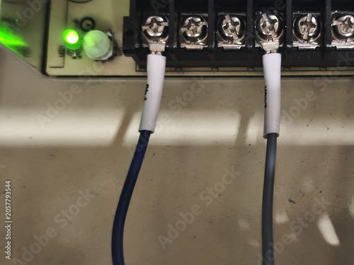 Electrical terminal block with connected wire, green indicator light on control panel, close up of industrial wiring installation