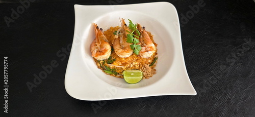 Pad Thai with fresh shrimp (Stir-fried Rice Noodles) served on white plate against black background. Arrange 3 large river prawns or tiger prawns on top. Noodles are coated with orange tamarind sauce
