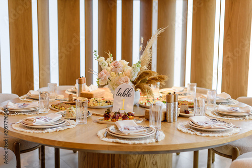 An elegant round wooden banquet table served for a wedding reception or gala event, decorated with a boho floral centerpiece and a golden Table 1 sign.