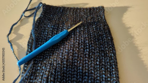 Blue crochet hook on dark shiny textured warm winter crochet project in soft lighting