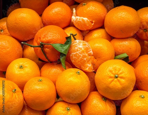 Vibrant heap of fresh, ripe clementines and tangerines, some peeled, with green leaves, showcasing natural textures and bright citrus colors in a close-up, high-detail studio shot.