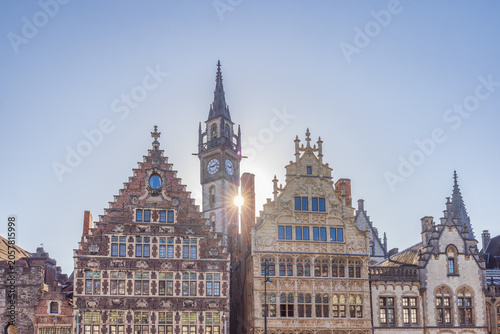 Ghent town in Belgium, Europe. Historic European city skyline with ancient architecture, bell tower, and a bright sunburst against a clear blue sky