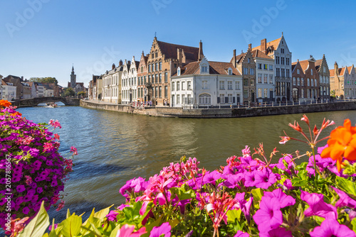 Bruges town in Belgium, Europe. Vibrant Floral Display Overlooking a Historic European Canal with Charming Gabled Buildings Under a Bright Blue Sky on a Sunny Day