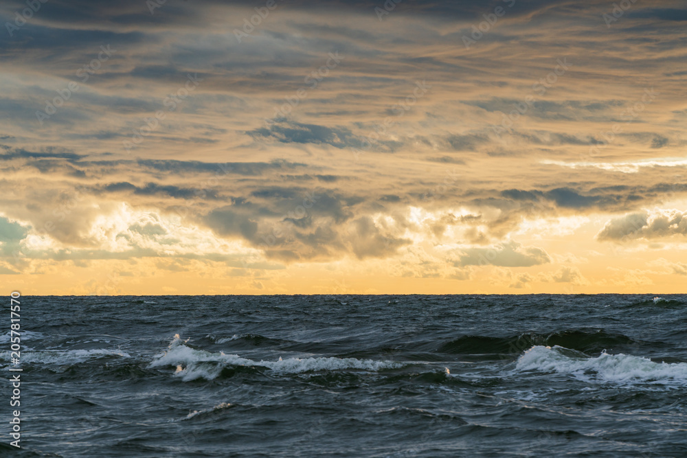 Obraz premium Dramatic ocean waves under a stormy, golden sunset sky