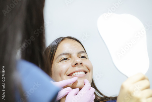 Woman smiling, seeing her healthy teeth in a mirror during dental checkup and consultation