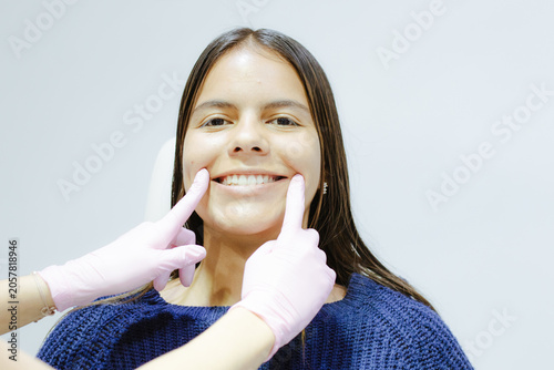 Young woman smiling during a dental checkup, doctor's gloved hands pointing at her perfect teeth