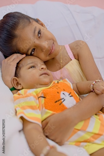 Sibling bond between girl and baby on a white bed in bright room