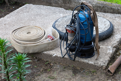 фотографія ​A professional blue submersible drainage pump with a wound cable and a fire hose prepared for work on a concrete manhole slab