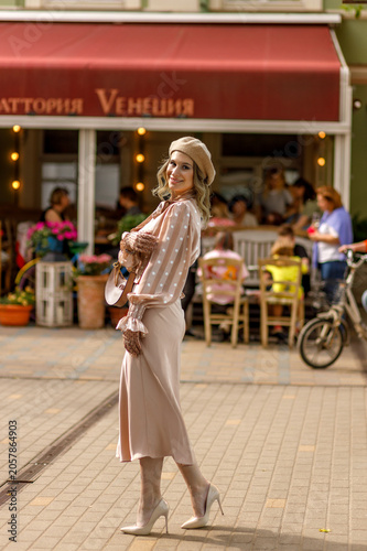 Portrait of a young blonde woman in a vintage pastel-colored outfit and a beret in the city center. Retro style.