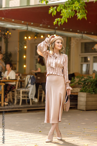 Portrait of a young blonde woman in a vintage pastel-colored outfit and a beret in the city center. Retro style.
