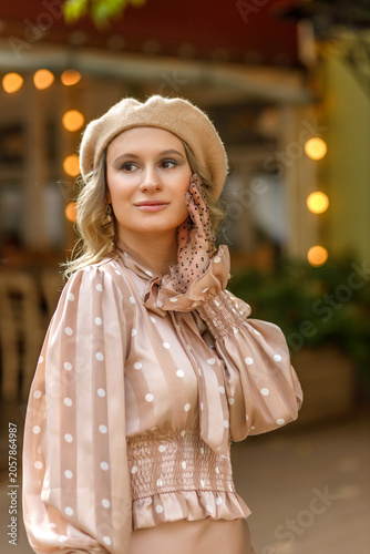 Portrait of a young blonde woman in a vintage pastel-colored outfit and a beret in the city center. Retro style.