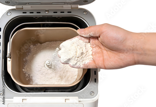Hand adding white flour into a mixing bowl for baking with electric mixer in use on a modern kitchen countertop