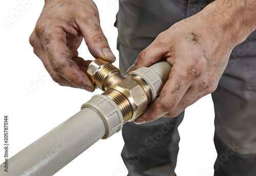 Close-up of a plumber tightening a brass valve on a gray PVC pipe for water supply system repair or installation, focusing on hands with dirty fingers and plumbing equipment