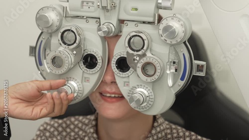 A positive female patient undergoes a professional vision check and refraction test using advanced ophthalmic equipment. This high-value commercial stock imagery represents preventative healthcare, pr