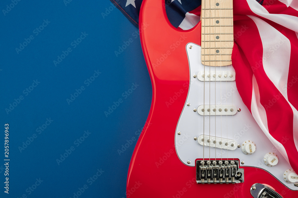 Fototapeta premium Red electric guitar with American flag on blue background. Patriotic music concept inspired by rock culture, live performance and American entertainment with copy space