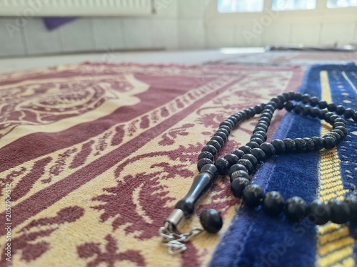 Black prayer beads resting on a patterned islamic prayer rug