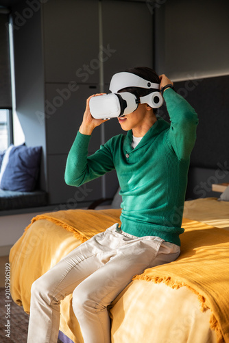 White virtual reality headset is being adjusted on bed in modern bedroom with mustard throw