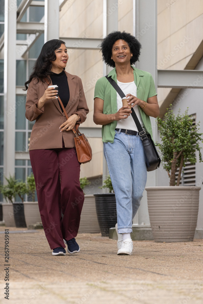 Fototapeta premium Diverse coworkers wearing smart casual walking by office building on path holding coffee and bags