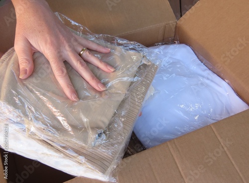 Closeup of woman's hands organizing and packing neutral-colored clothing into a cardboard box. E-commerce product packaging or unpacking concept.