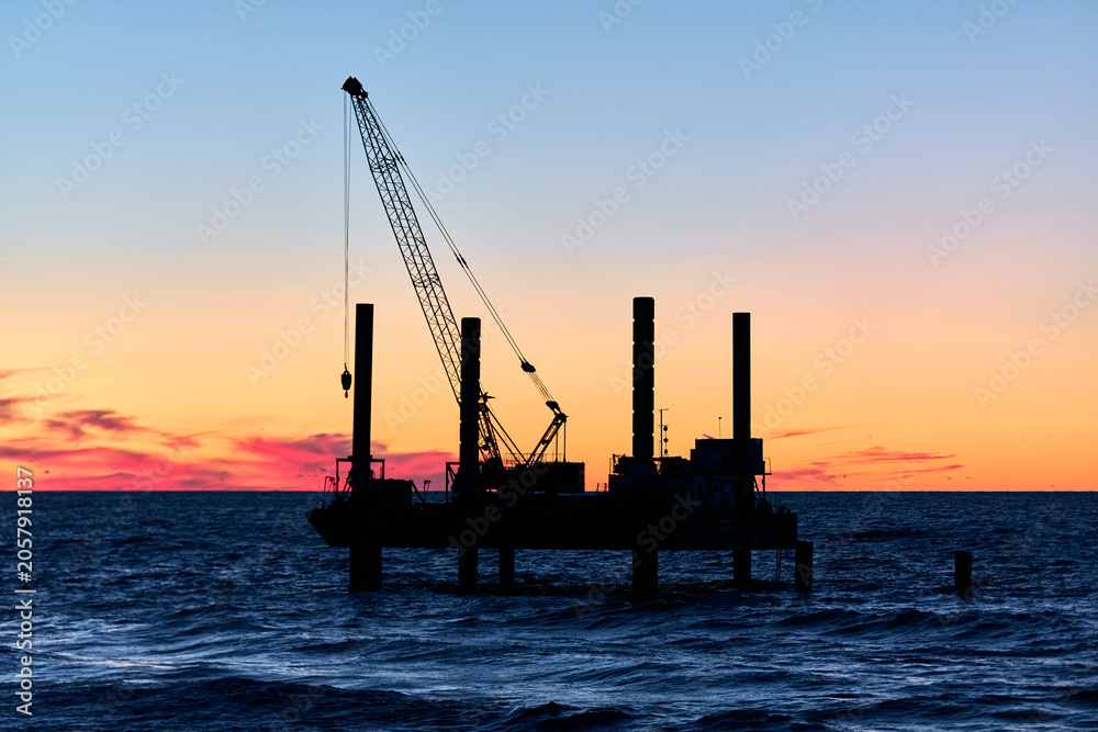 Obraz premium Offshore crane platform silhouette at sunset over calm ocean waters