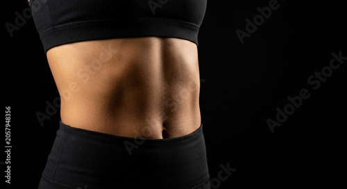 Close up of fit woman muscular belly on black background
