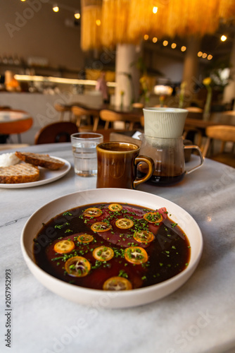 A dish of tuna is served in a bowl at a restaurant. The background shows drinks and slices of bread on a table. It is a casual dining setting with soft lighting.