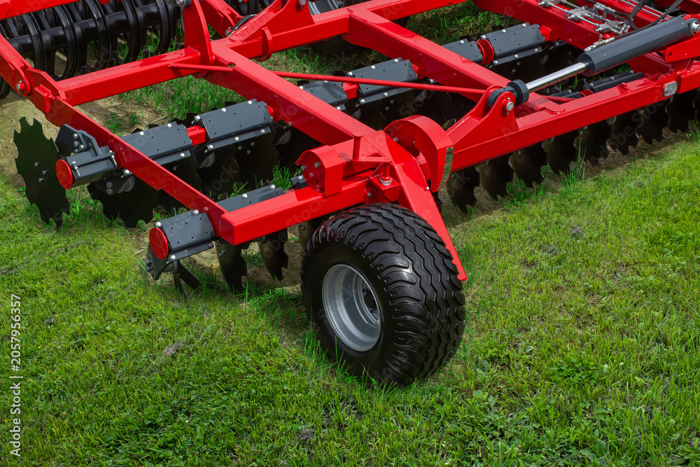 Obraz premium Red agricultural disc harrow rests on lush green grass
