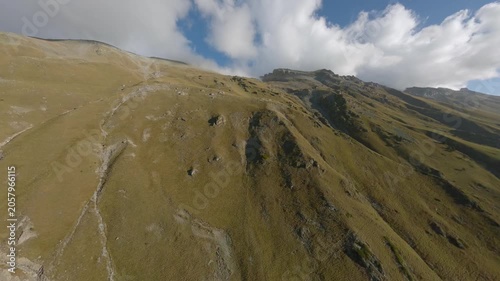 Fast FPV drone flight skimming along a dry alpine ridge toward a rugged mountain peak wrapped in low clouds. Cinematic aerial movement reveals steep slopes, rocky terrain, and wild highland scenery