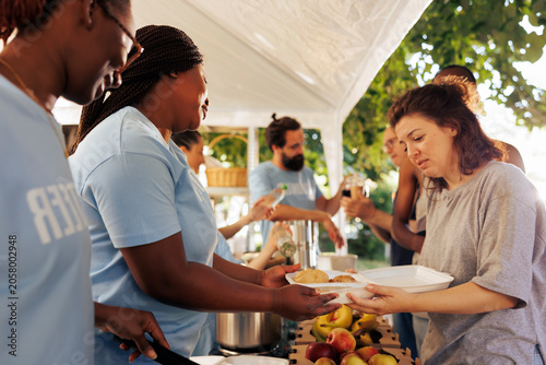 Hunger relief team of volunteers donates essential items and free food to needy, showing generosity in serving less fortunate. Non-profit outdoor food bank sharing warm meals to poor homeless people.