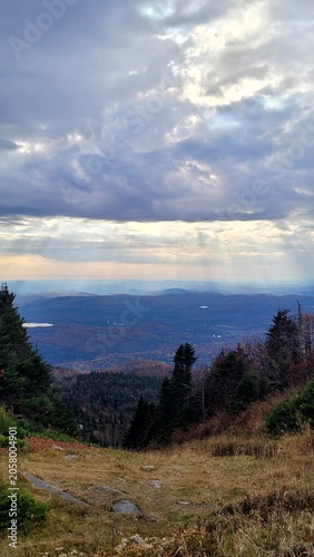 Breathtaking mountain view of autumn forest valley with sun rays breaking through dramatic clouds