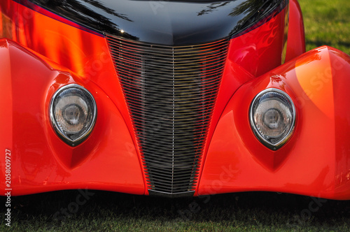 Front View of Red Vintage Automobile Detail - Close-up view of the front grille and headlights of a red vintage automobile.
