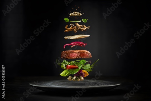 Gourmet steak with floating ingredients stacked above a black plate. Creative culinary composition of meat, mushroom, vegetable and herb. Fine dining food concept for restaurant menu.