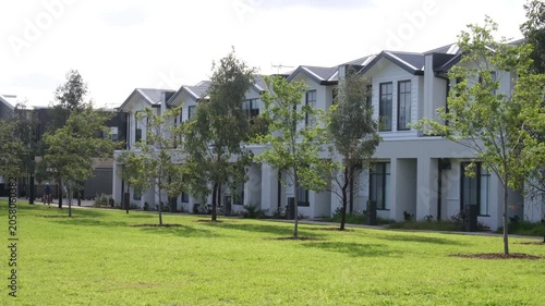 A row of modern two-storey townhouses facing a green parkland reserve in a new residential estate,Truganina, Melbourne, Australia. A child rides a bicycle along a footpath in the distance