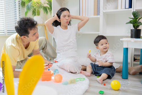 
Warm sunlight streams through blinds. Family of three smiles softly in cozy room. Mother holds infant close, father looks lovingly on. Green plant adds freshness to minimalist shelves

