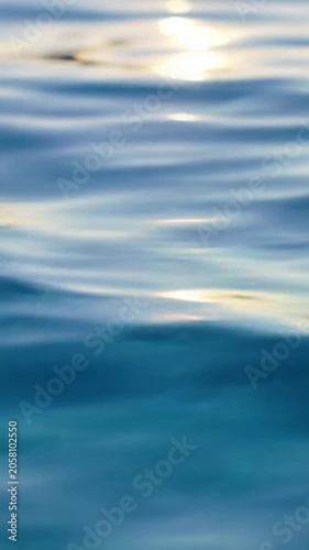 Extreme macro video, eye-level, of pristine deep blue water surface with undulating ripples, subtle golden hour reflections, and delicate caustics, slow dolly in. Concept of natural balance and purity