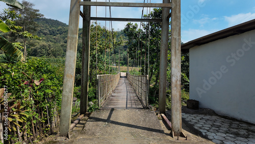 An open pathway leads to swings surrounded by lush greenery and distant hills under a blue sky