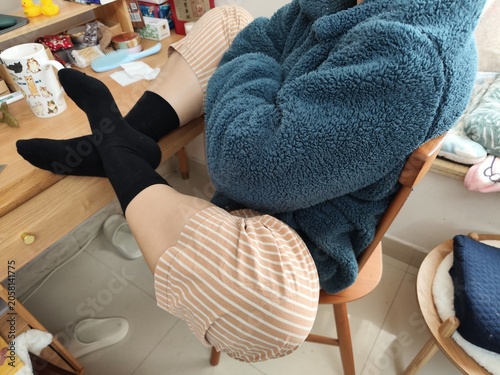 Cozy indoor scene of person in blue fleece robe and striped shorts sitting at wooden desk, wearing
