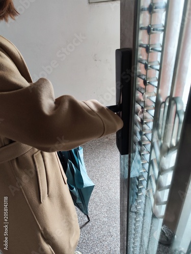 Woman in beige coat installing smart door lock on metal security gate in urban apartment entrance,