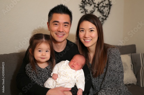 Happy Asian Family with Newborn Baby and Toddler Daughter at Home