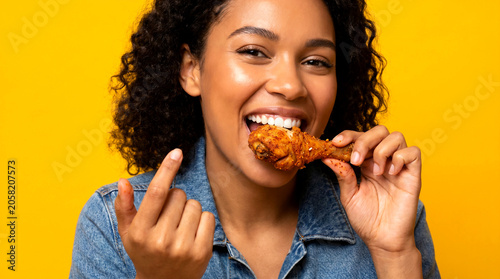 woman smiling and eating a crispy fried chicken drumstick against a bright yellow background