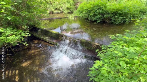 Water gently falling from a small dam and flowing downstream, steady footage