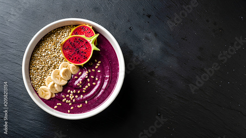 A vibrant acai smoothie bowl topped with banana slices, dragon fruit, and oats on a dark textured surface.