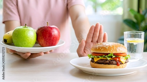 Person making a healthy food choice, holding a plate of fresh apples and banana while rejecting a hamburger, concept of diet decision, nutrition awareness and avoiding junk food.