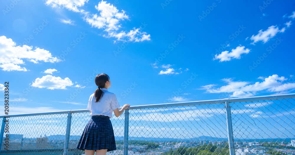 Naklejka premium 屋上フェンスから青空を見上げる女子高校生の後ろ姿