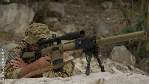 Canvastavla A military sniper in camouflage lies in a concealed position, aiming his advanced rifle with a scope during a tactical surveillance operation in the mountains