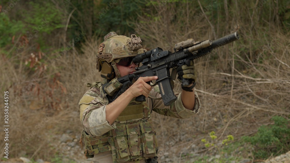Fototapeta premium A special forces soldier in full combat gear advances during a tactical mission, aiming his assault rifle while patrolling a rugged, hostile environment.