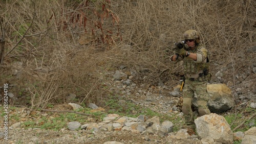 Photos A special forces operator in full combat gear secures a perimeter while patrolling through rugged, hostile wilderness terrain for a military operation