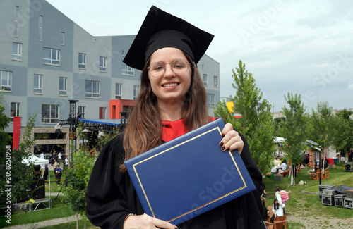 young female graduate holding diploma on the background of graduation ceremony